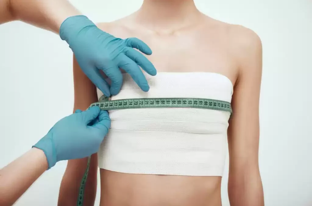A woman measures her breasts with a measuring tape to ensure proper relaxation of chest muscles after breast augmentation.