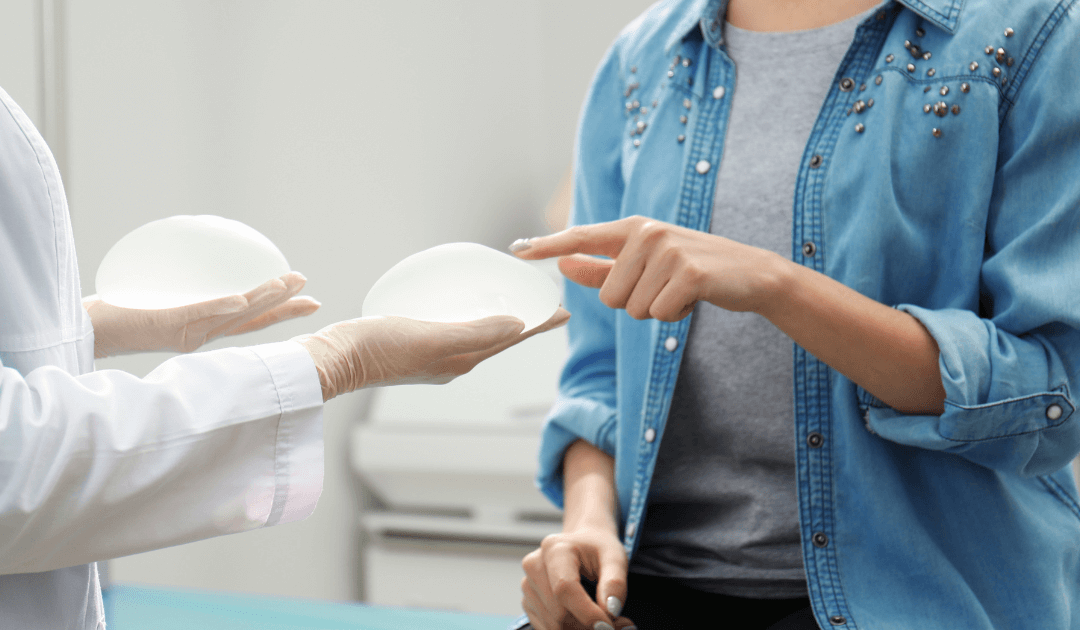 Plastic surgeon showing silicone breast implants to a female patient during consultation and explaining recovery time.