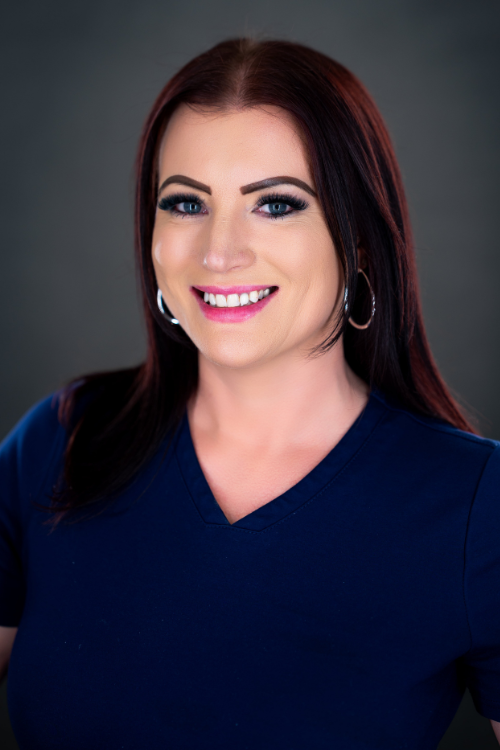Woman with long dark hair, wearing a navy blue top and hoop earrings, smiling at the camera against a plain dark background. Woman with long dark hair, wearing a navy blue top and hoop earrings, smiling at the camera against a plain dark background.