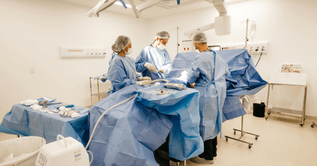 Why Las Vegas Is a Top Destination for Plastic Surgery Tourism 1 Three surgeons in blue gowns and masks perform an operation in a brightly lit operating room, highlighting Las Vegas plastic surgery as a top destination for those seeking plastic surgery tourism.