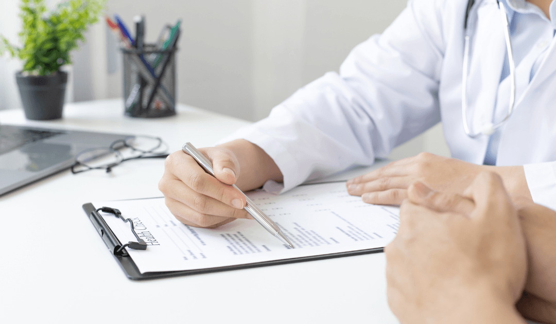 A doctor in a white coat reviews a breast lift (mastopexy) medical form on a clipboard with a patient across the desk, discussing options for the procedure in Las Vegas.